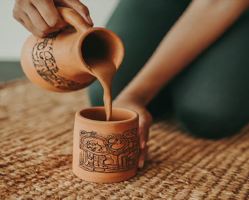 A person preparing a frothy chocolate drink in a traditional Mesoamerican ceremony.