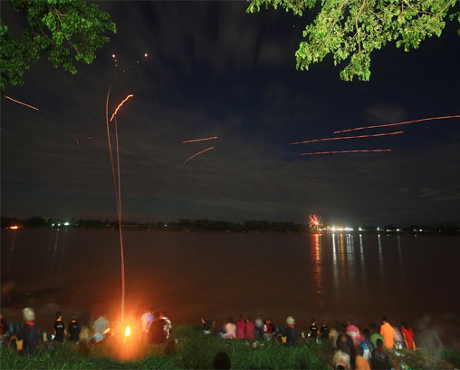 The tracks of two Naga fireballs (at left) rising vertically into the sky before petering out near the top of the photo. The other tracks are of sky lanterns or fireworks.
