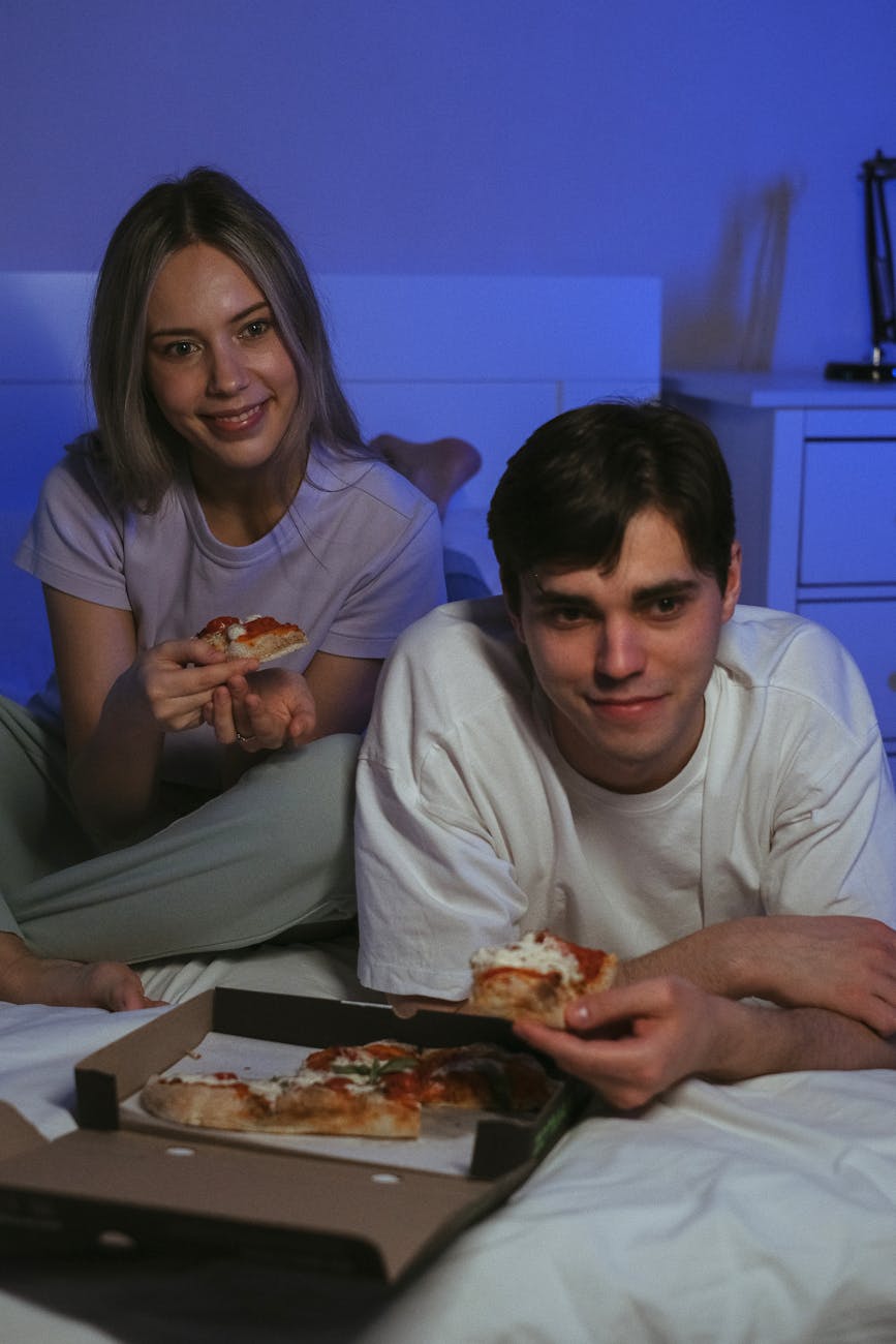 Una pareja comiendo pizza en la cama