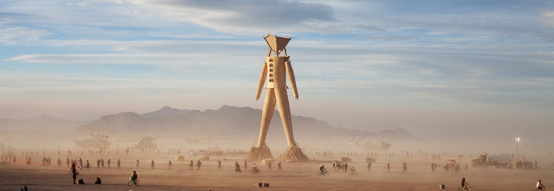 people walking around wooden statue of man in desert