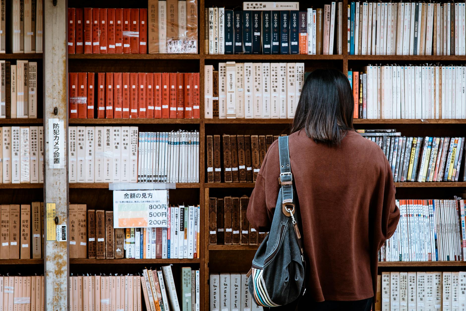 Mujer con camisa marrón que lleva una bolsa de cuero negro frente a los libros de la biblioteca