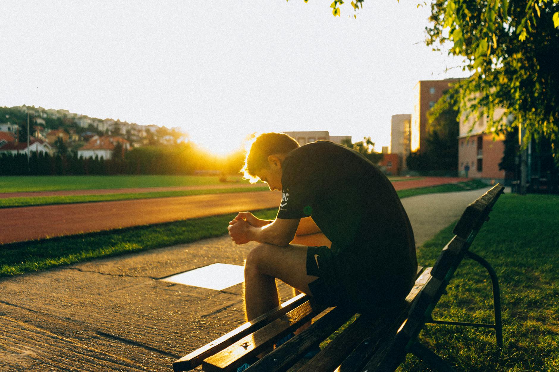 hombre sentado en un banco cerca del campo de atletismo mientras el sol se pone