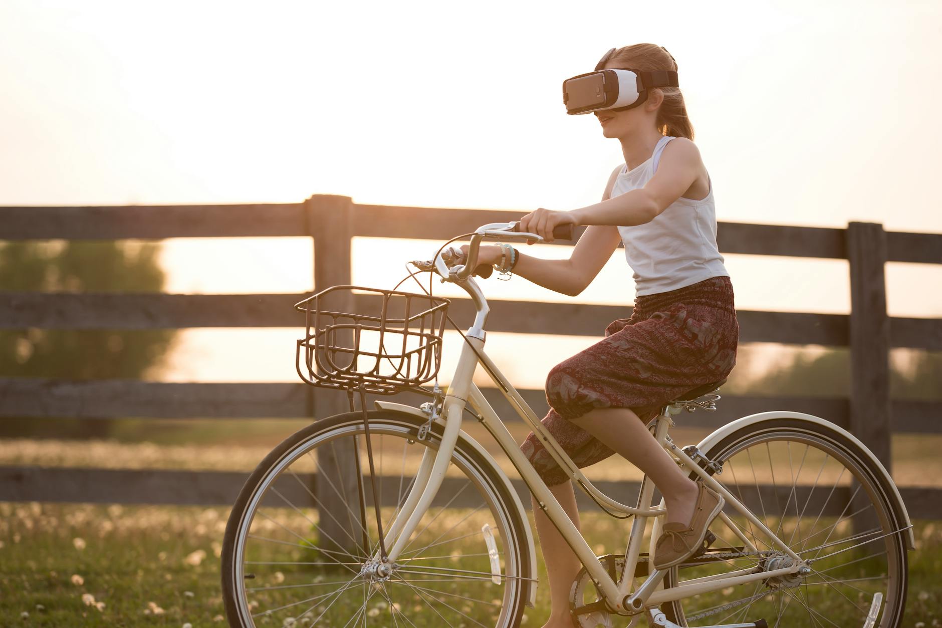 Muchacha que lleva la caja de VR conduciendo la bicicleta durante la hora dorada