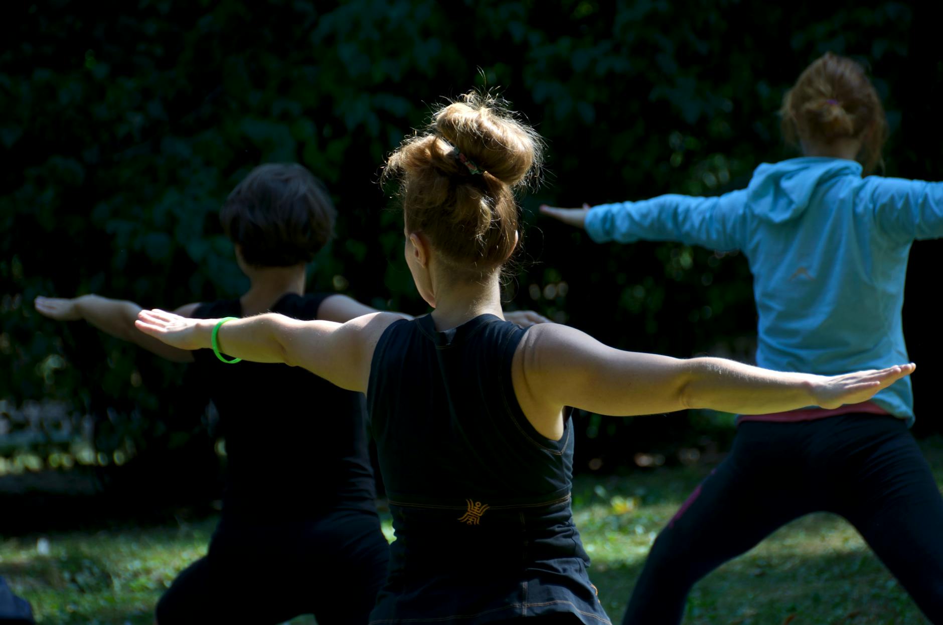 Mujeres irreconocibles realizando la asana Warrior II durante una clase de yoga al aire libre en el parque