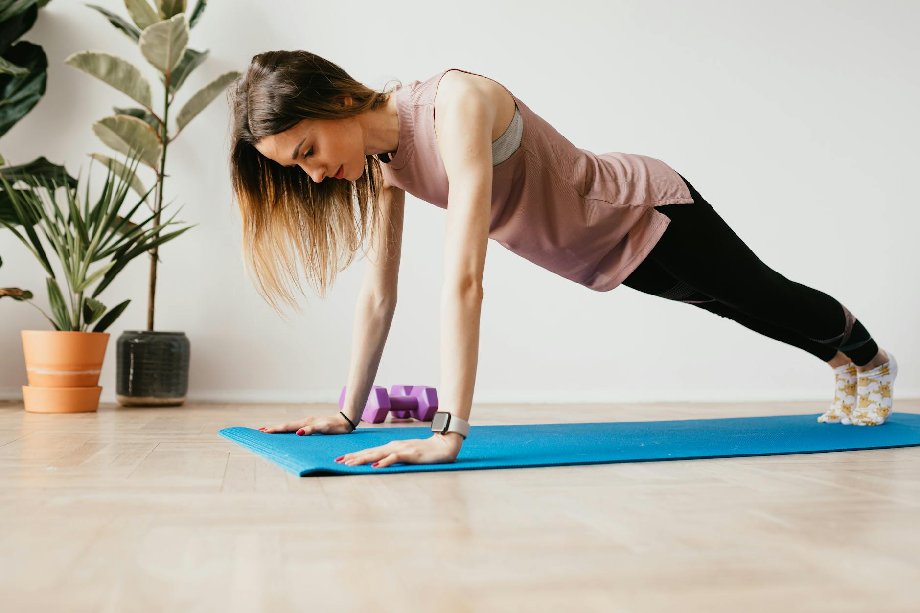 fit woman in smart watch standing in plank pose indoors