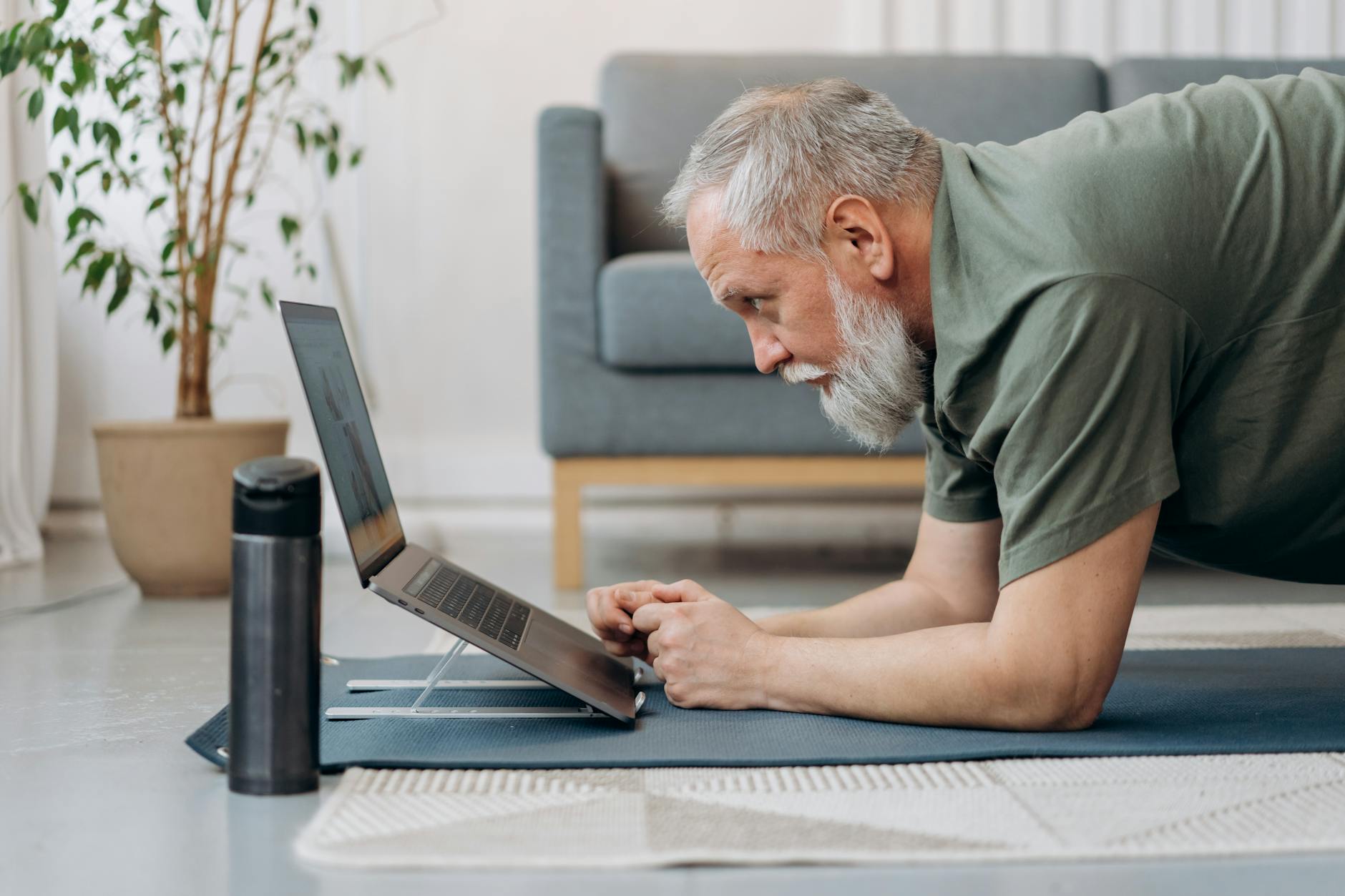 Un anciano haciendo ejercicio mientras mira la computadora portátil