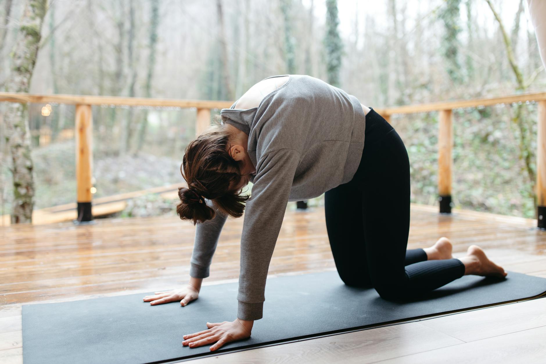 Mujer con camisa gris de manga larga y leggings negros haciendo yoga sobre esterilla de yoga negra