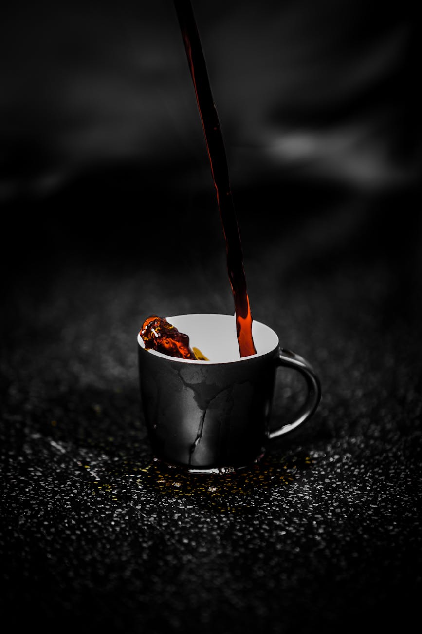 liquide brun se déversant sur une tasse en céramique noire et blanche photographie couleur sélective