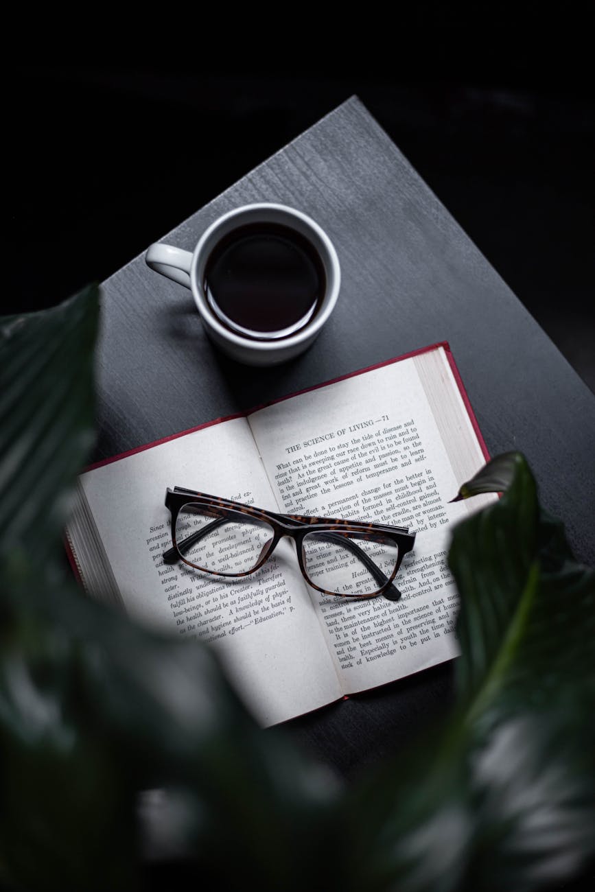 lunettes sur un livre ouvert à côté d’une tasse de café sur la table