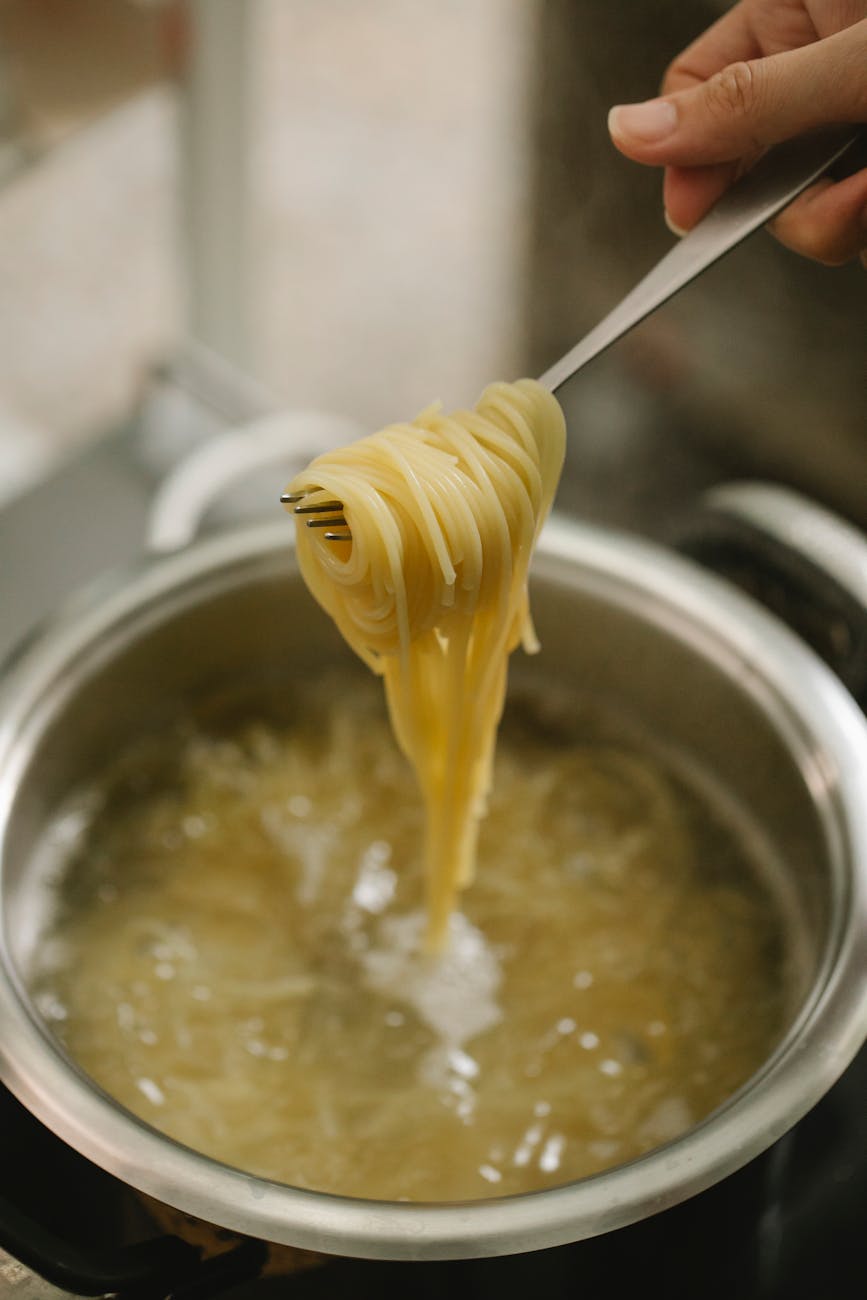 Crop Sans Visage Chef Montrant Fourchette Avec Spaghetti Au-dessus D’une Casserole