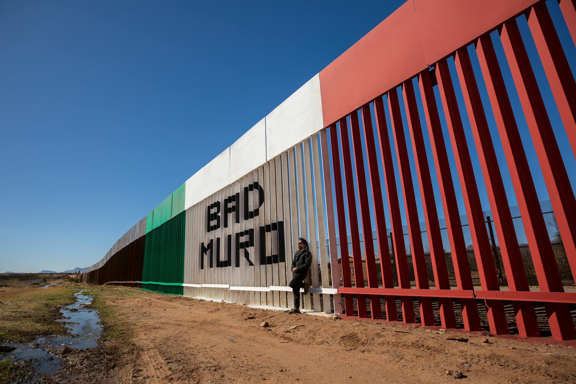 Hombre de pie contra la pared en la frontera de EE.UU. y México con un letrero Bad Muro Naco, Sonora, México